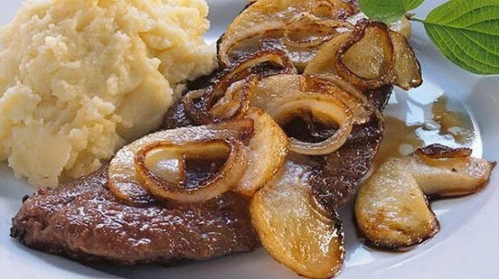 Leber mit Zwiebeln auf einem Teller, serviert mit Beilagen