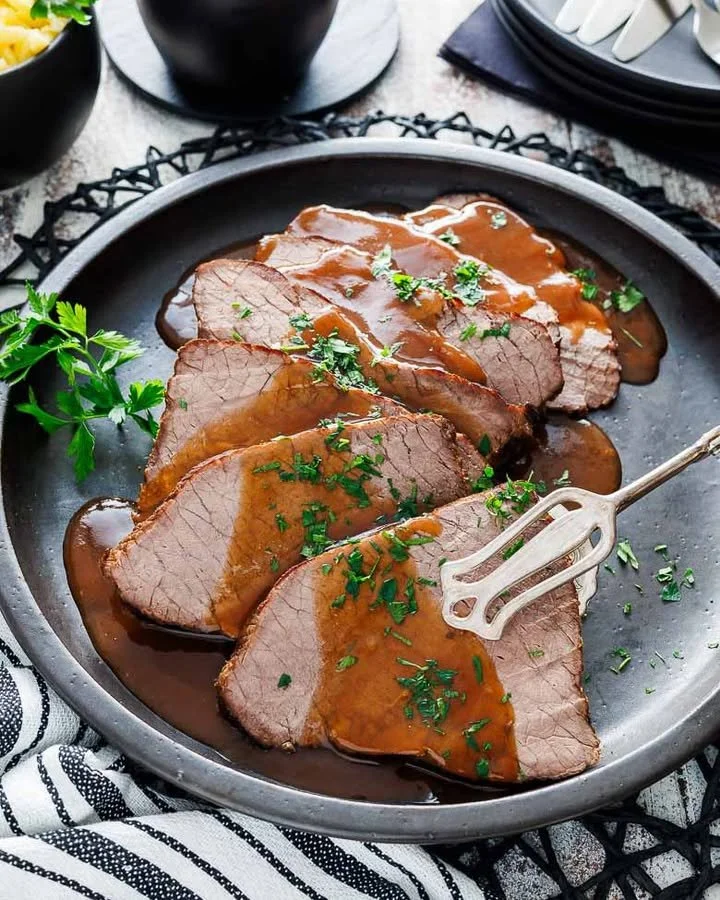Delizioso Rinderbraten mit Soße auf einem Teller serviert.