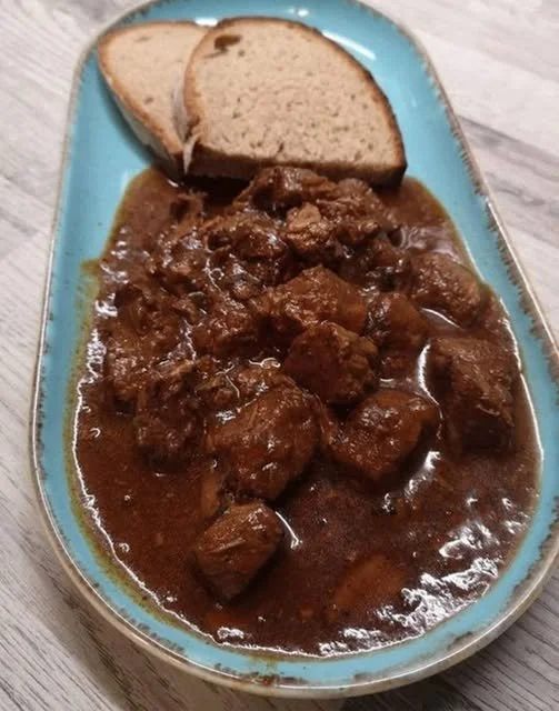 Wiener Gulasch serviert mit Beilagen auf einem Teller.