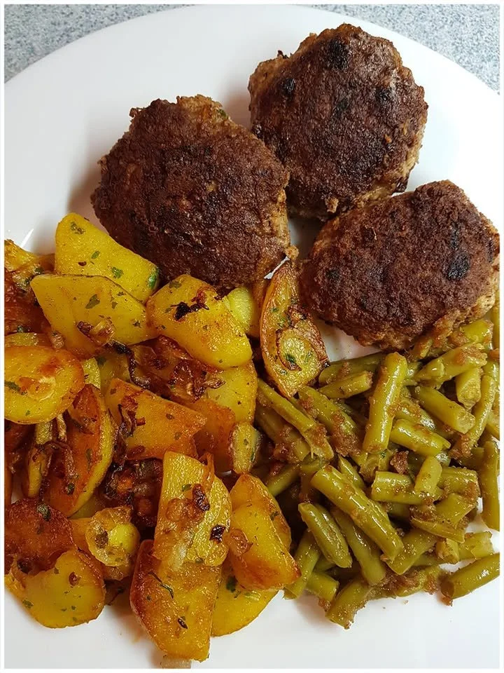 Bouletten mit Bratkartoffeln und Bohnen auf einem Teller angerichtet