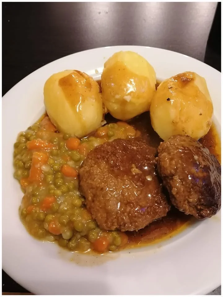 Frikadellen mit Salzkartoffeln, Erbsen und Möhren auf einem Teller serviert.