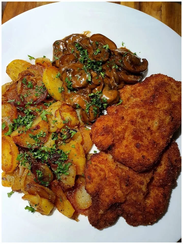 Schnitzel mit Champignon-Sahne-Soße und Bratkartoffeln auf einem Teller angerichtet.